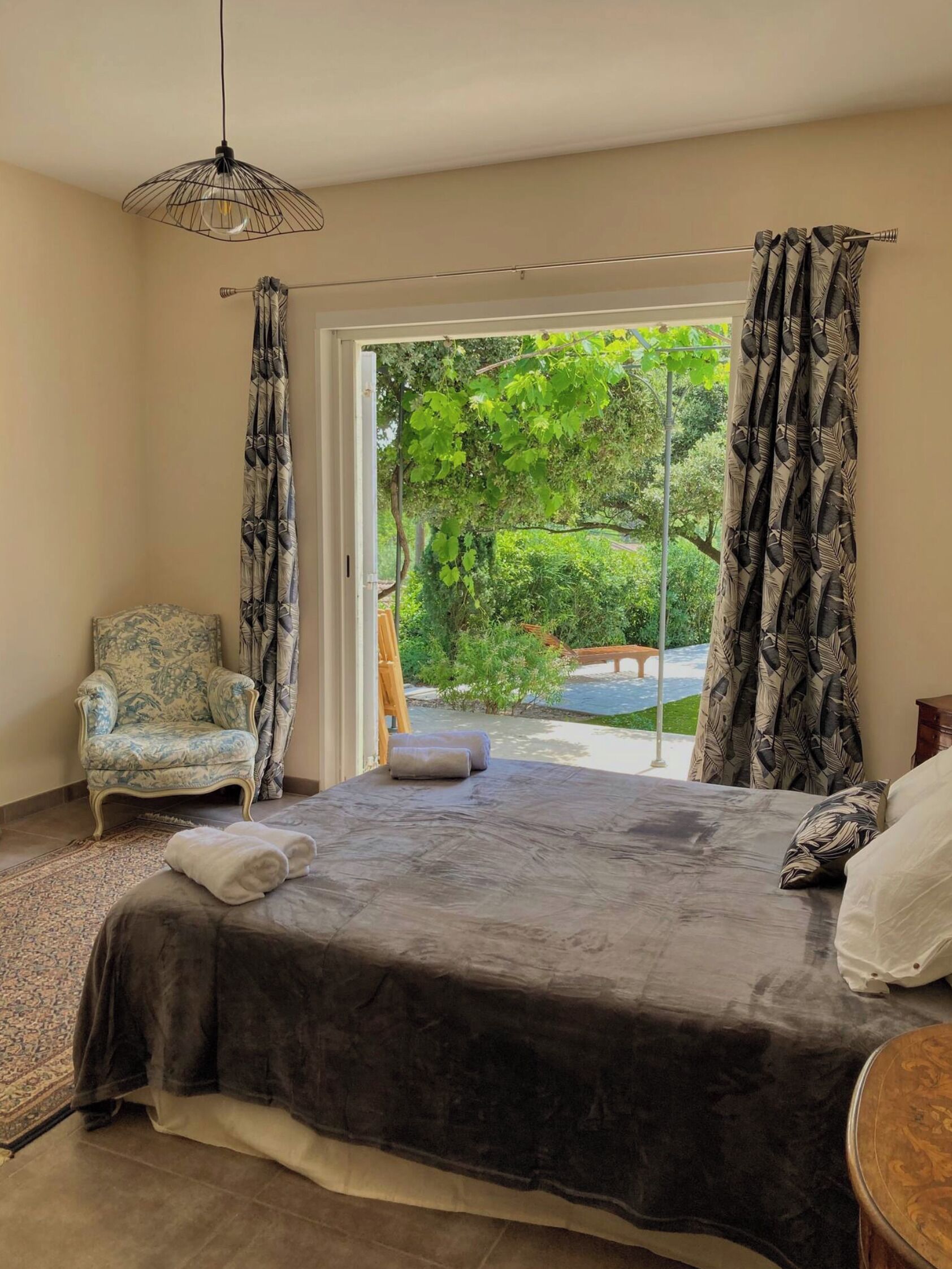 A bedroom with a bed, a chair, and a view of a garden through a sliding door.