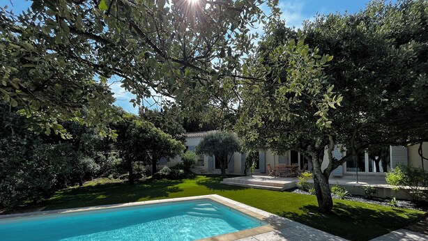 A swimming pool surrounded by lush greenery and a building with outdoor seating. - Candau Villa, a green haven with a wooded garden and a pool, 5min from Avignon (Les Angles)