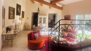 A spacious living room with a wooden ceiling, a dining area with a table and chairs, and a view of the kitchen through an open doorway. - Candau Villa, a green haven with a wooded garden and a pool, 5min from Avignon (Les Angles)
