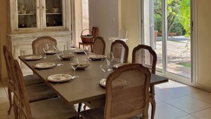 A dining room with a large table set for six, surrounded by wicker chairs. - Candau Villa, a green haven with a wooded garden and a pool, 5min from Avignon (Les Angles)