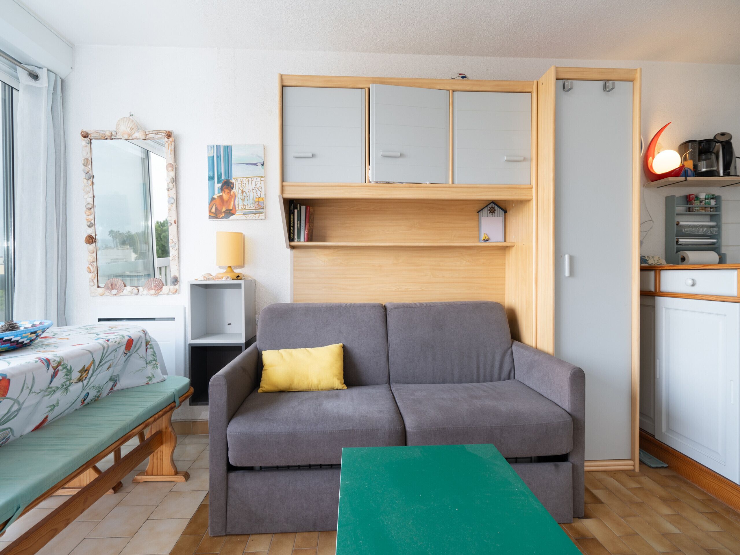 A compact living space with a grey sofa, a small table, a wooden cabinet, and a window with curtains.