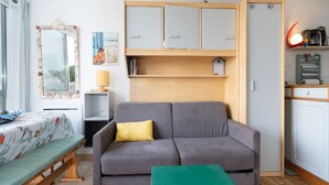A compact living space with a grey sofa, a small table, a wooden cabinet, and a window with curtains.