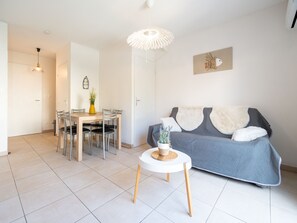 Uma sala de estar moderna com um sofá cinzento, uma mesa de centro branca e arredondada, e um espaço de jantar com mesa e cadeiras de madeira.