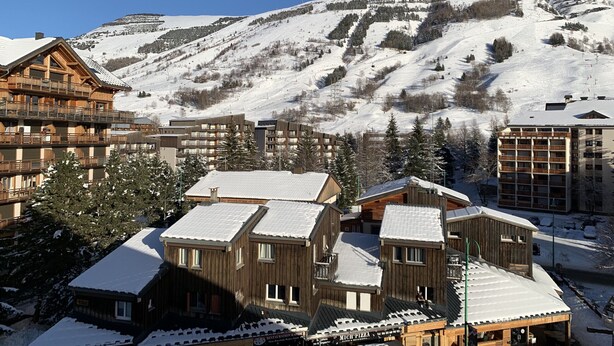 A snow-covered mountain resort with wooden buildings, ski slopes, and a clear sky. - Nice  apt on high floor with lift for 6 people (Les Deux Alpes)
