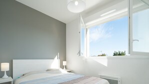 A modern bedroom with a bed, bedside tables, a window, and a radiator. - Villa with garden near the beach for 6 pers (Sérignan)