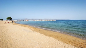 A beach with clear blue water, a sandy shore, and a distant rocky breakwater. - Ampelas Nostalgia Apartments - Zeus Haven in Paros (Ampelas)