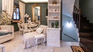 A cozy living room with a white sofa, a small white table, and a Christmas tree. There is a white cabinet with decorative items and a mirror above the table.