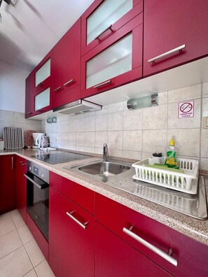 A modern kitchen with red cabinets, a stainless steel sink, and a dish rack. - Holiday apartment Sonja with great terrace, near the beach and center (Krk)