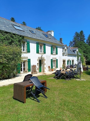 A white building with green shutters, a covered outdoor seating area, and a lawn. - Beautiful Secluded Converted Breton Farmhouse with Pool
Generous grounds/gardens (Leuhan)