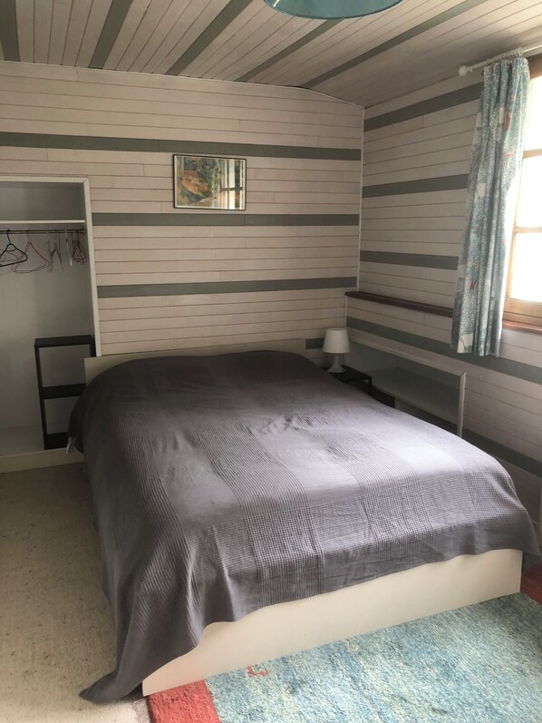 A bedroom with a bed, a wardrobe, a small table, and a window with curtains. - Beautiful Secluded Converted Breton Farmhouse with Pool
Generous grounds/gardens (Leuhan)