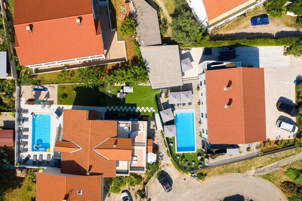 Vista aérea de un barrio residencial con dos piscinas, varias casas y una zona de estacionamiento.