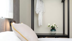 Habitación de hotel con una cama, una bata blanca colgada en la pared y un florero con flores blancas sobre una mesita de noche.