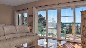 Un salon avec un canapé beige, une table basse en verre et une vue sur un balcon aménagé avec du mobilier d’extérieur.