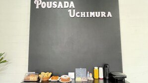 En svart tavla med texten ”POUSADA UCHIMURA”, en disk med bakverk, olika tillbehör och en kaffemaskin.