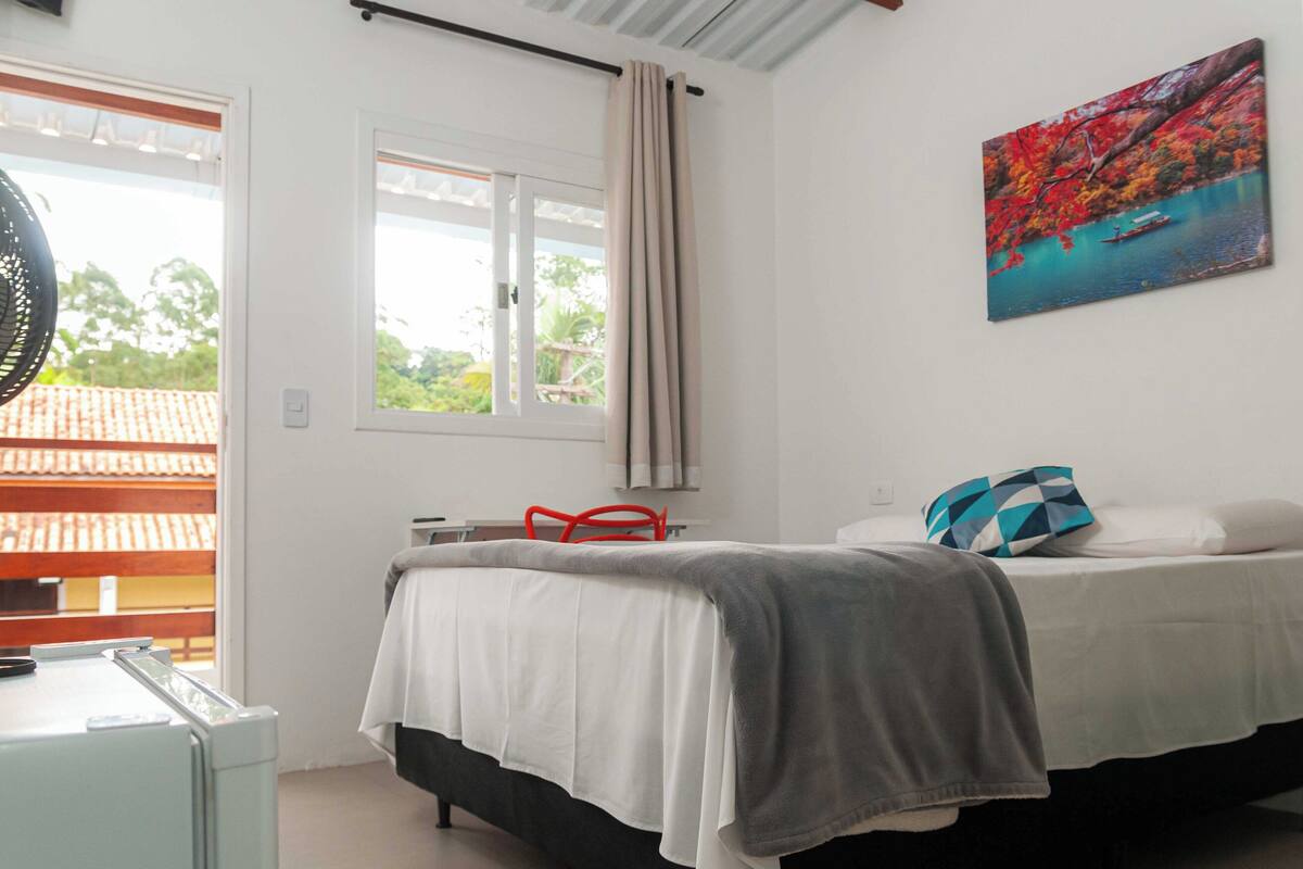 Un dormitorio con cama, ventana, cuadro y ventilador.