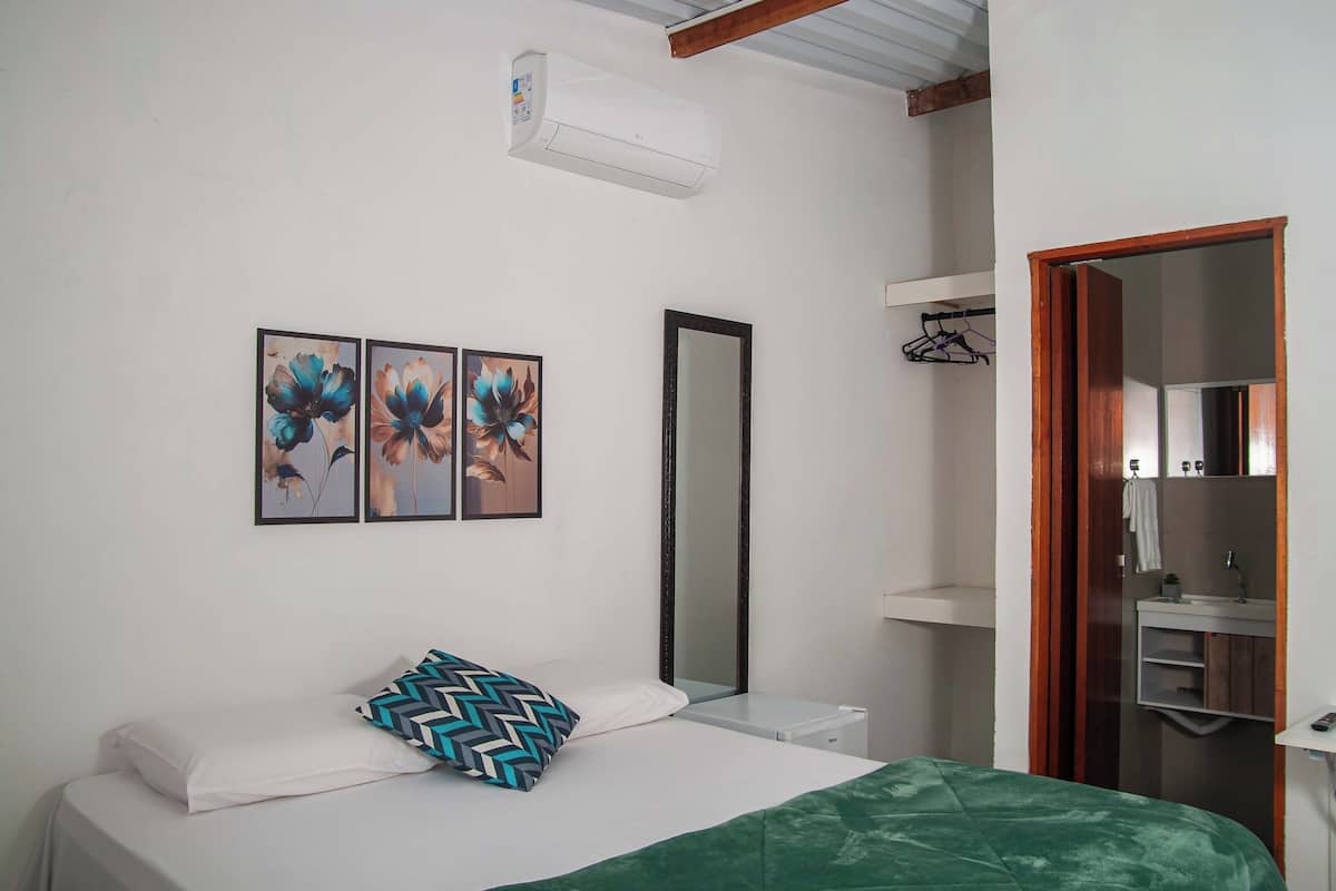 Un dormitorio con cama, mesita de noche, espejo y cuadros colgados en la pared.