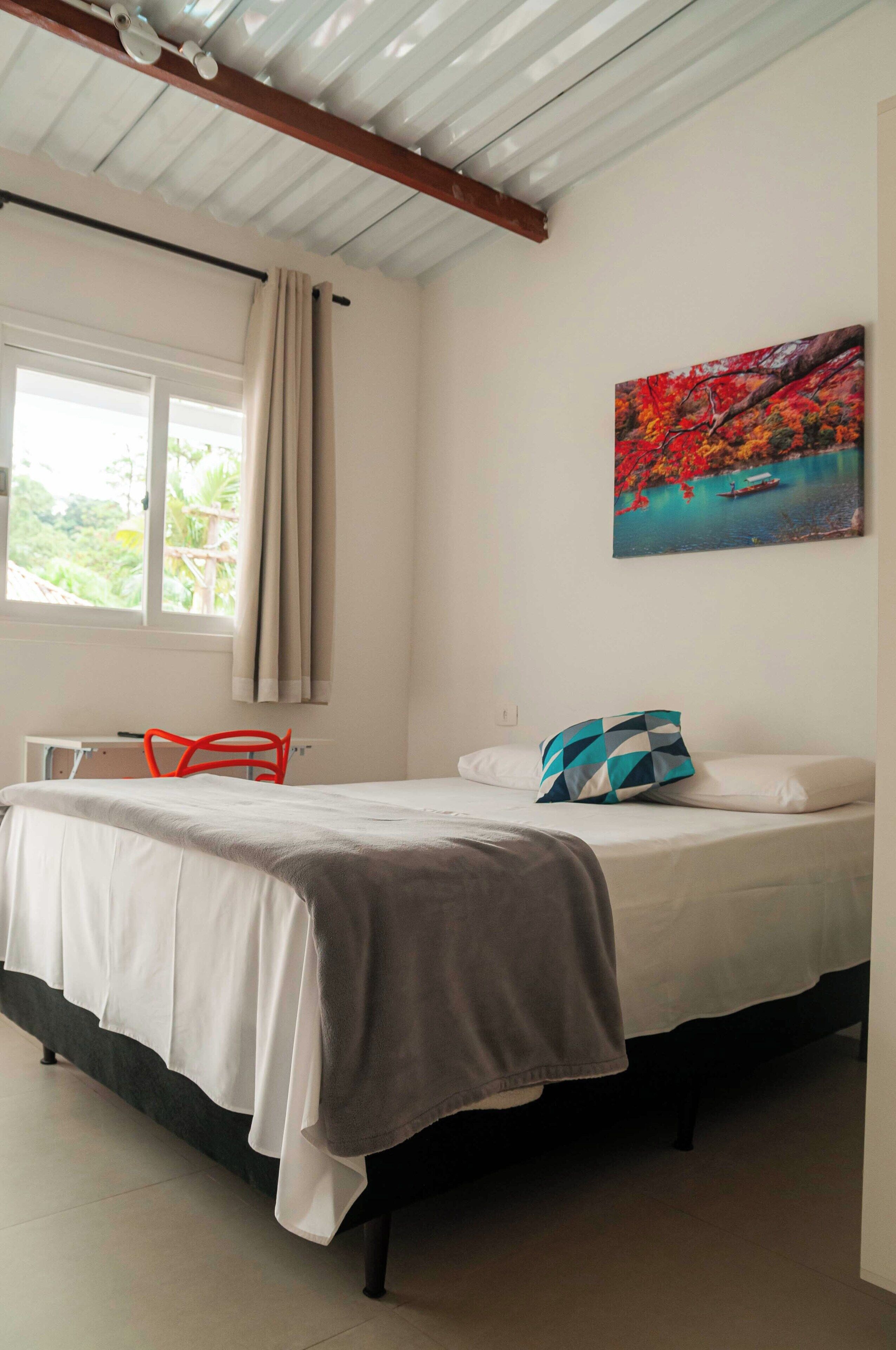 Une chambre à coucher avec un lit, une fenêtre avec des rideaux, une chaise et un tableau accroché au mur.