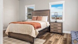 Un dormitorio con cama, mesita de noche, lámpara, ventana con vistas y ventilador de techo.
