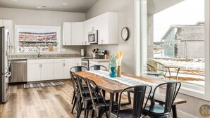 Una cocina moderna con armarios blancos, una mesa de comedor de madera y vistas a un paisaje nevado.