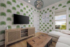A living room with a flat-screen TV, wooden entertainment unit, and a large window with a view of the outdoors.