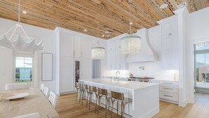 A modern kitchen with white cabinetry, a large island with bar stools, and a wooden ceiling. - Luxury Sound-View Escape with Private Pool, Hot Tub, and Stunning Amenities! (Pensacola Beach)