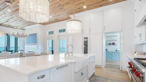 A modern kitchen with white cabinetry, a large island, stainless steel appliances, and a chandelier. - Luxury Sound-View Escape with Private Pool, Hot Tub, and Stunning Amenities! (Pensacola Beach)