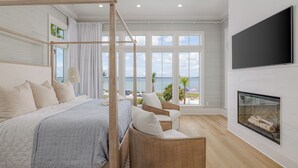 A bedroom with a large bed, a wicker chair, a fireplace, and a TV. - Luxury Sound-View Escape with Private Pool, Hot Tub, and Stunning Amenities! (Pensacola Beach)