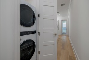 A hallway with a washing machine and dryer, a white door, and a view of the outside.