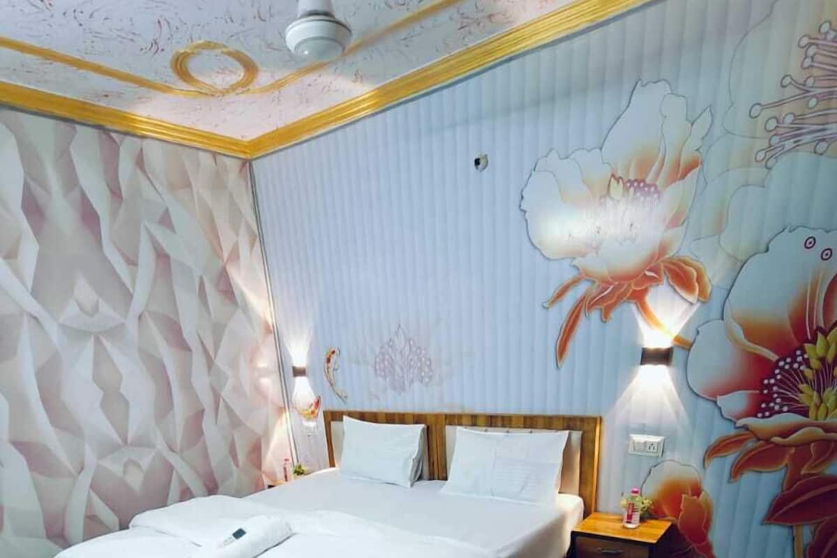 Une chambre à coucher comprenant un lit, une table de chevet, une lampe fixée au mur et une fresque murale à motifs floraux.