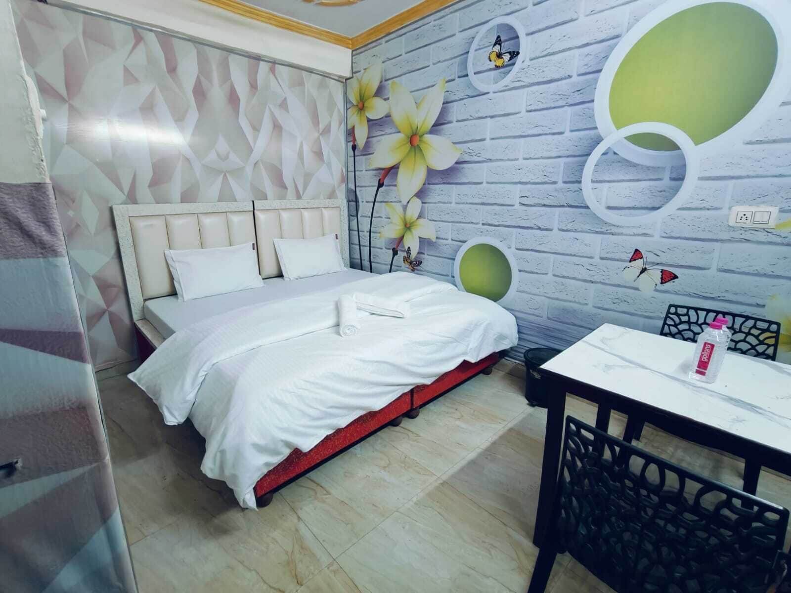 Een hotelkamer met een bed, een klein tafeltje en een stoel. Op de muren zijn decoratieve elementen te zien, zoals bloemen en vlinders.