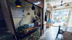 A cafe with a wooden counter, a whiteboard with operating hours, and a view of the street outside. - Milestone Homestay Agra (Agra)