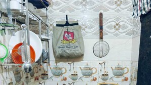 A kitchen with a gas stove, hanging utensils, a gas cylinder, and a trash bin. - Milestone Homestay Agra (Agra)