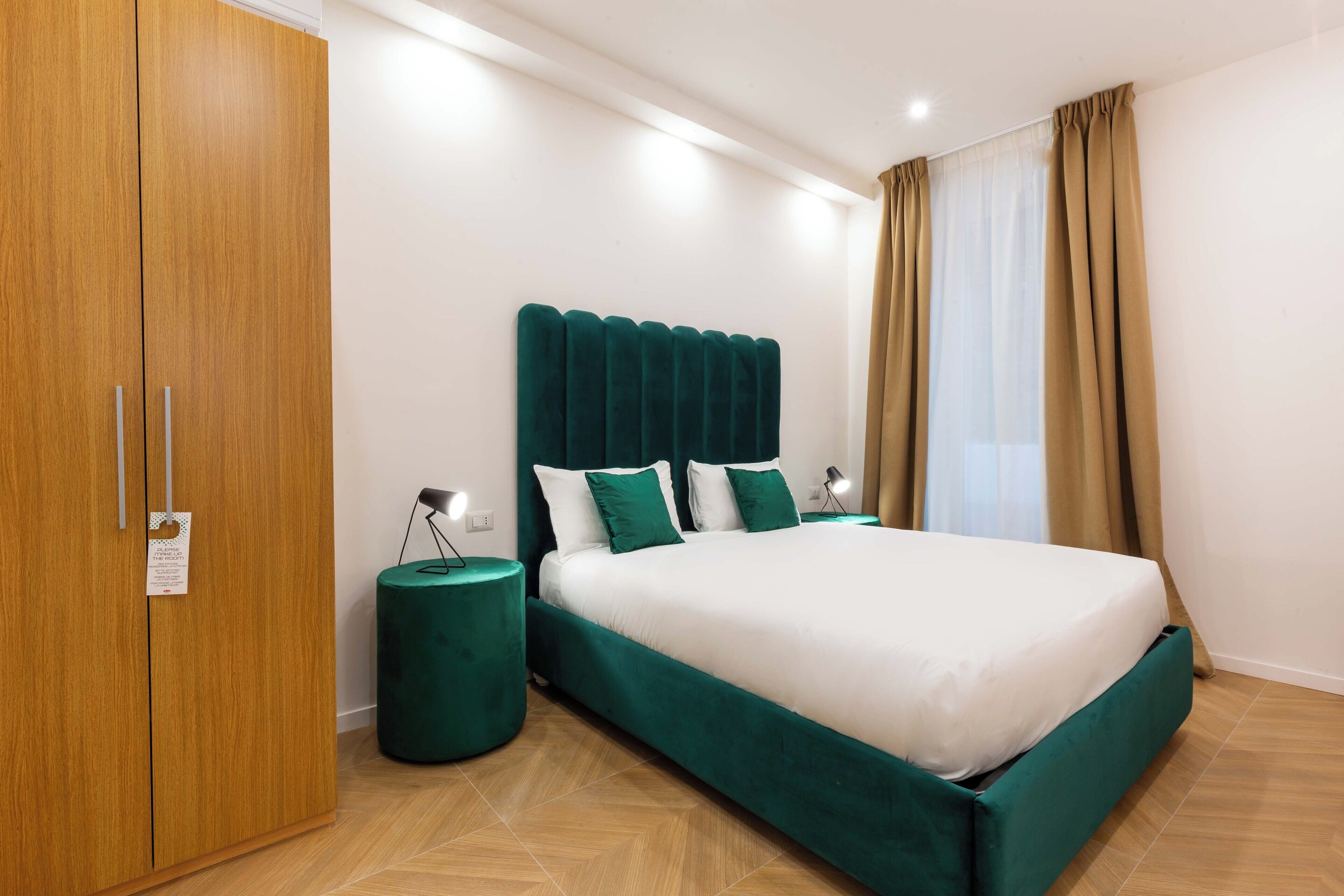 Une chambre à coucher avec un grand lit, une armoire, une table de chevet ronde et une fenêtre avec des rideaux.