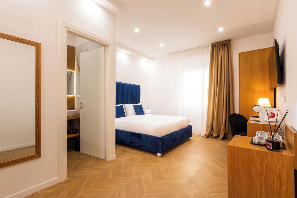 A hotel room with a bed, a wooden desk, a television, and a wardrobe.