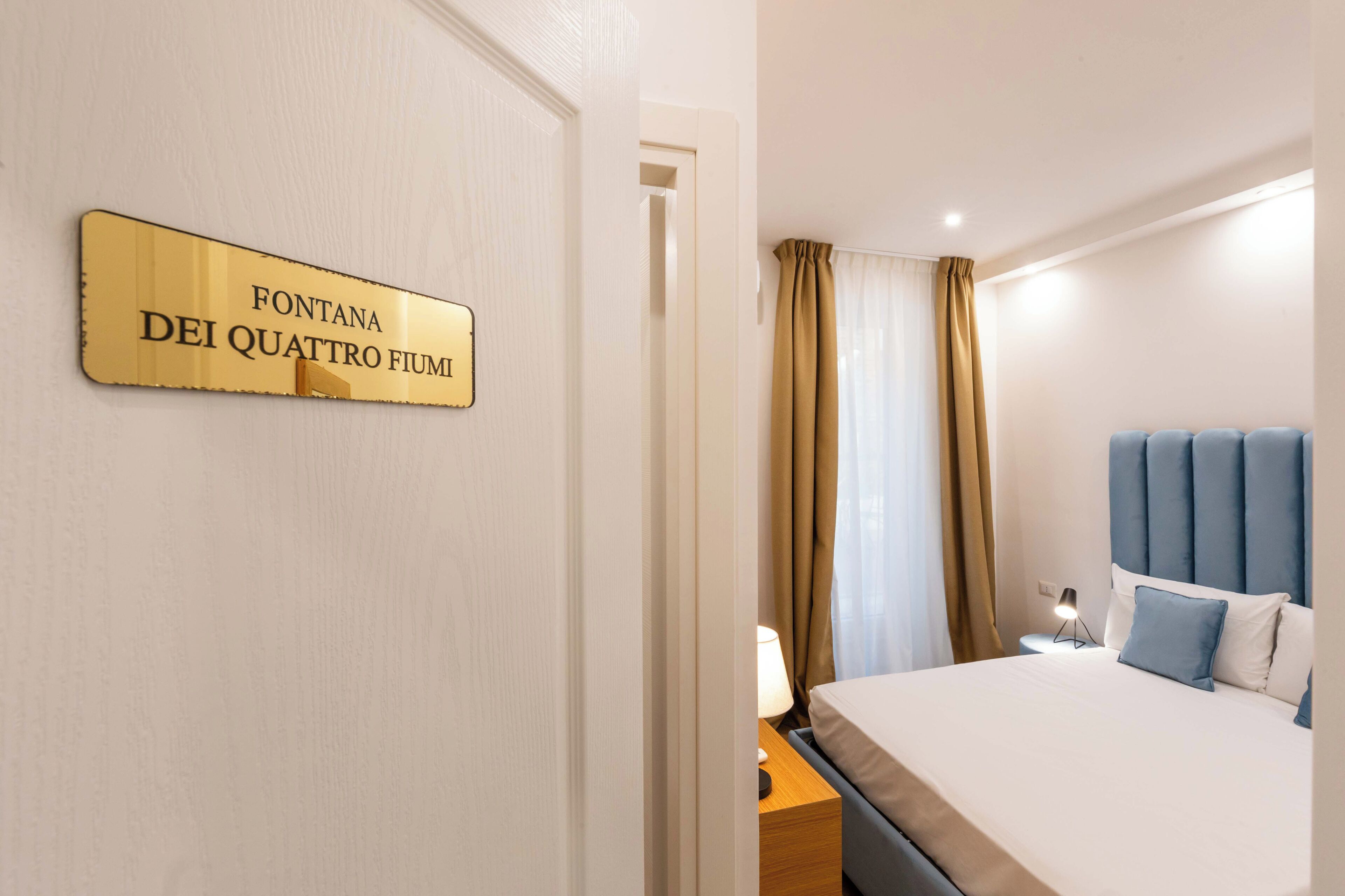 Et hotelværelse med en seng, et natbord, en lampe og et skilt på væggen.