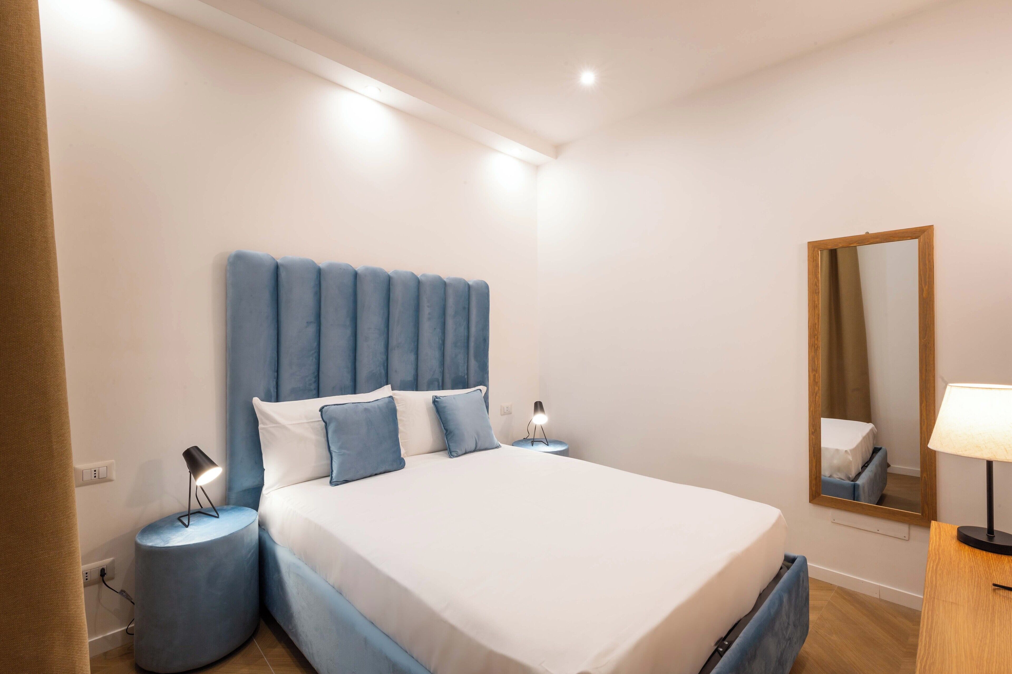 A bedroom with a bed, two bedside tables, a nightstand, a mirror, and a lamp.
