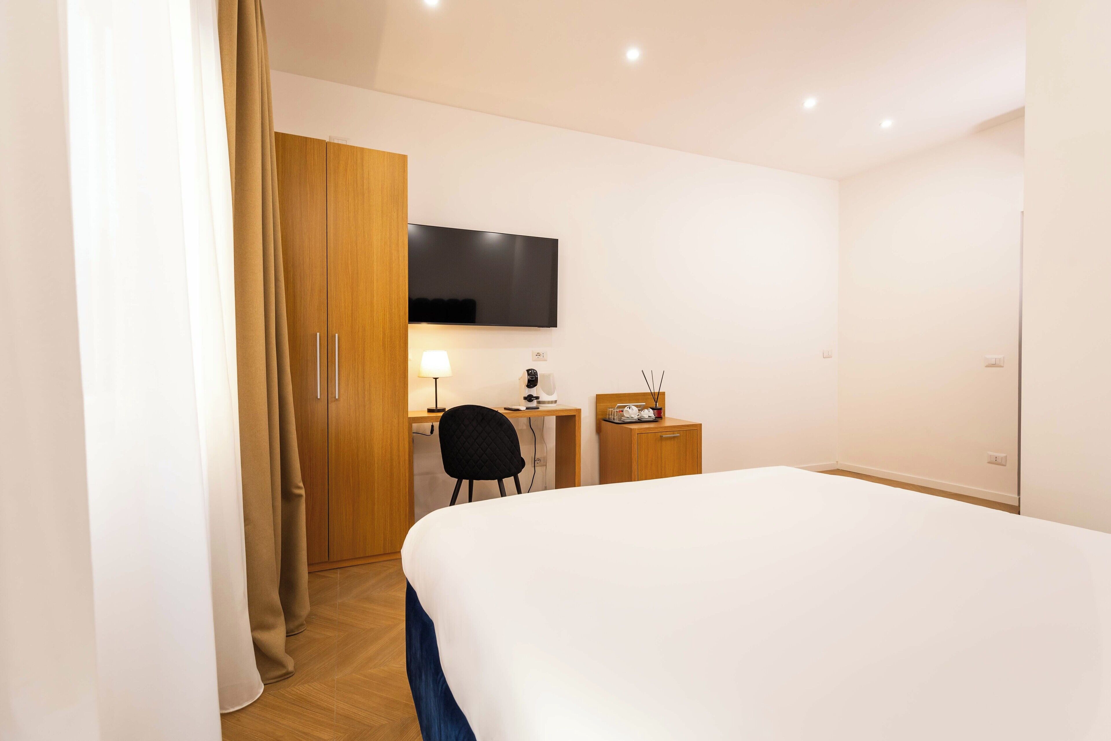 Una camera d'albergo con un letto, una scrivania con una sedia, un televisore e un piccolo armadio.