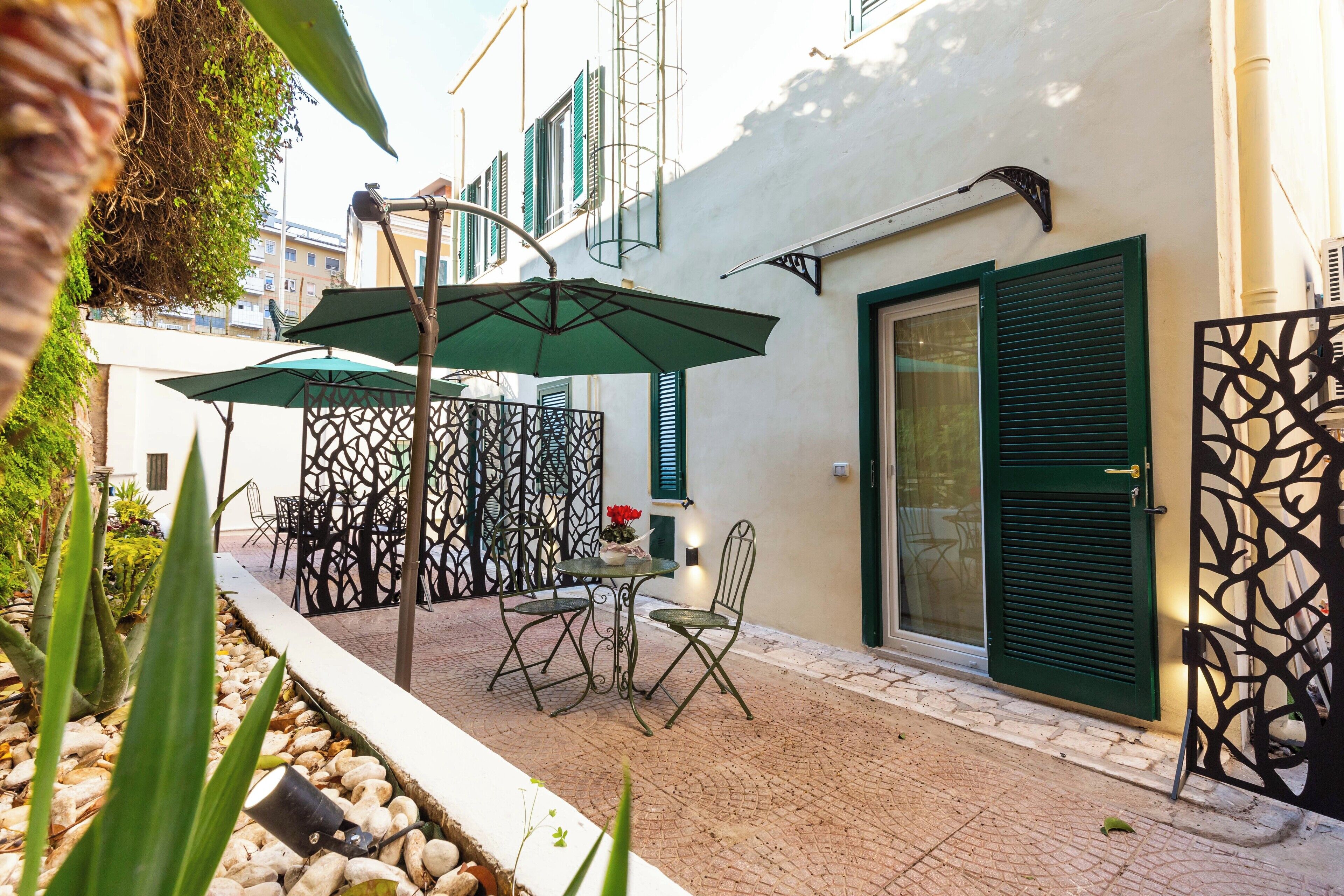 An outdoor patio area with a table and chairs, a decorative metal fence, and a building with green shutters.
