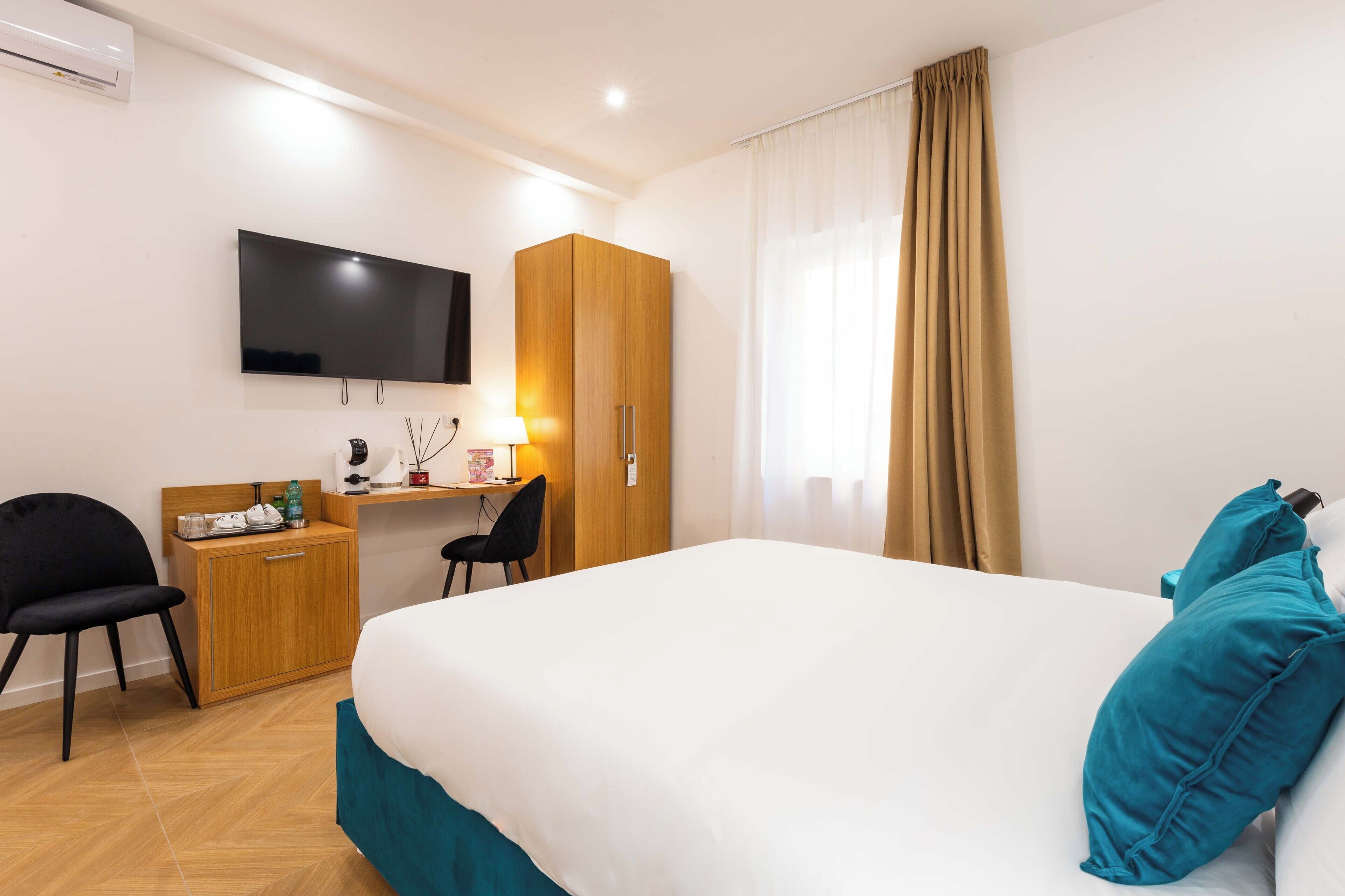 Ein Hotelzimmer mit einem Bett, einem Schreibtisch mit Stuhl, einem an der Wand befestigten Fernseher und einem Kleiderschrank.