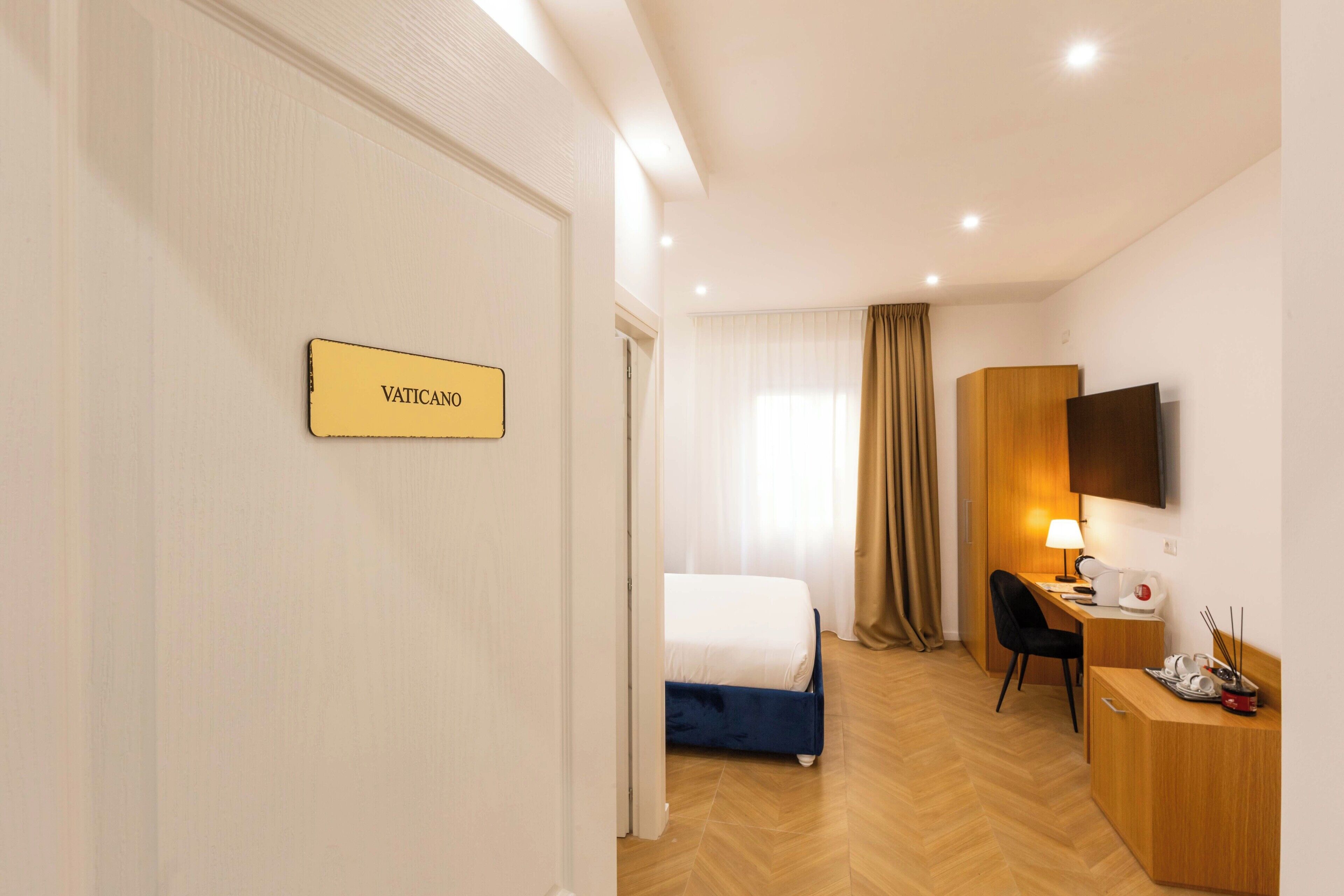 A hotel room with a bed, desk, chair, and a TV mounted on the wall.
