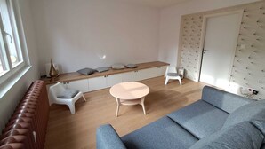 Un salon moderne avec un canapé, une petite table ronde et un banc. Un radiateur se trouve à gauche et une armoire au motif matelassé, à droite.