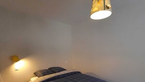 Une chambre à coucher avec un lit, une lampe fixée au mur et une petite fenêtre.
