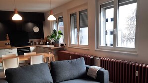 Un salon moderne avec un canapé gris, une table à manger en bois et un coin cuisine équipé d’une cuisinière et de placards.