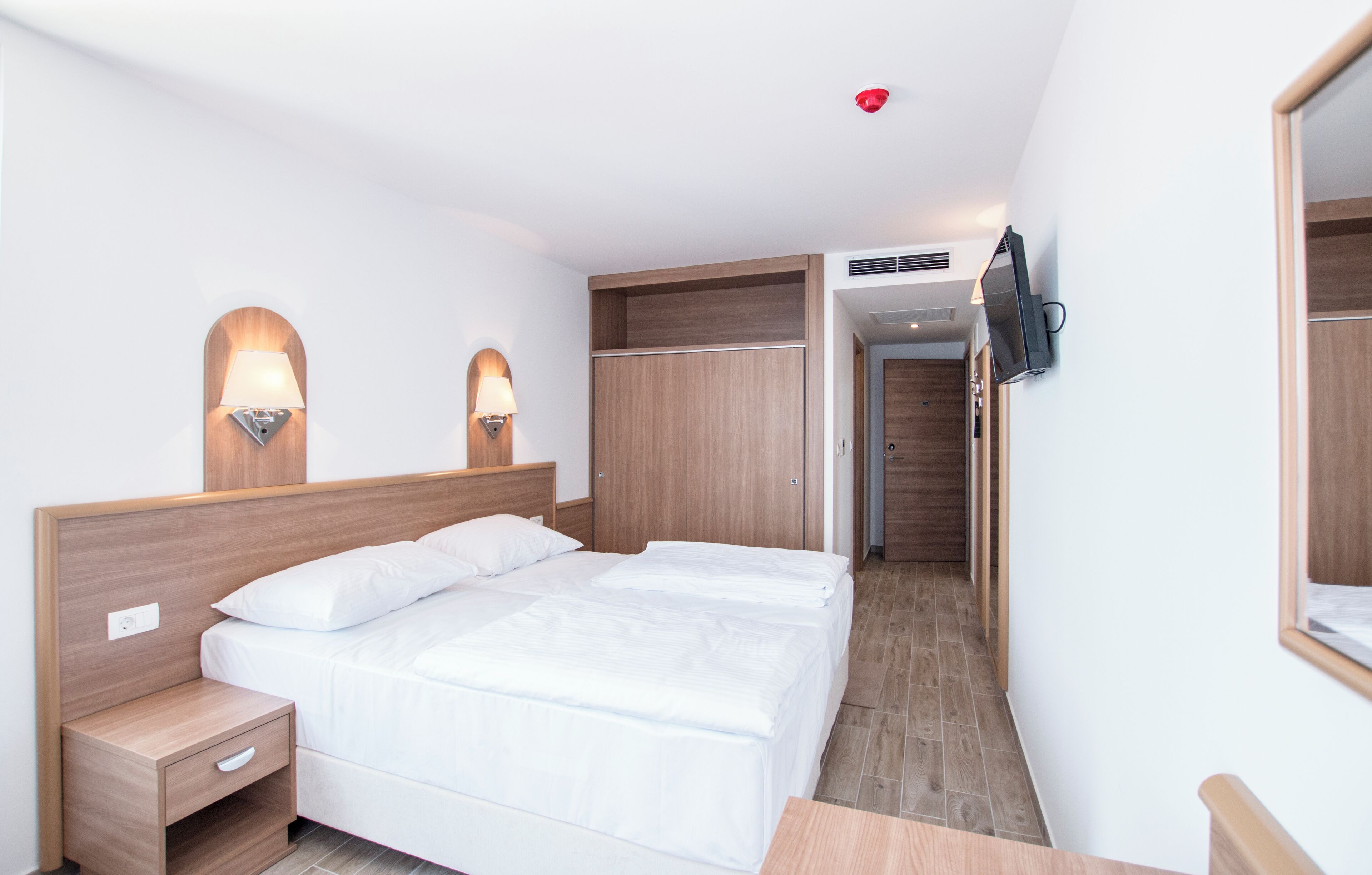 A hotel room with a bed, nightstands, a TV, and a wardrobe.