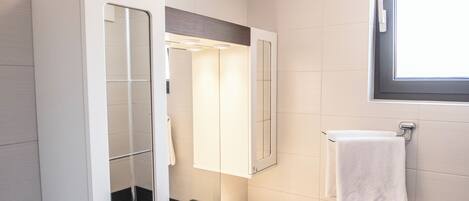 A modern bathroom with a white vanity, a large mirror, a sink, and a window above the mirror.