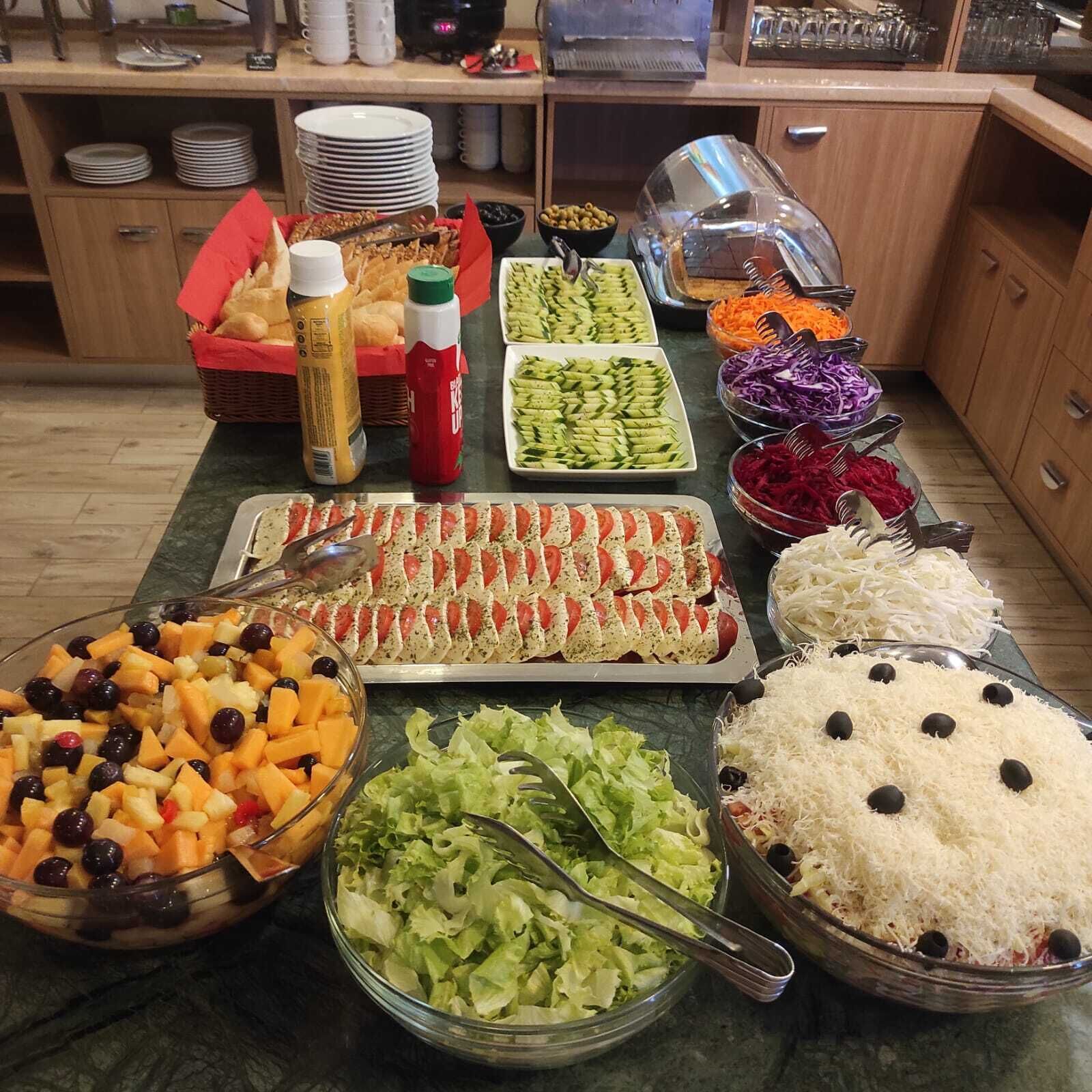 Una mesa de buffet con diferentes opciones de comida, como ensaladas, frutas y una bandeja de sándwiches.
