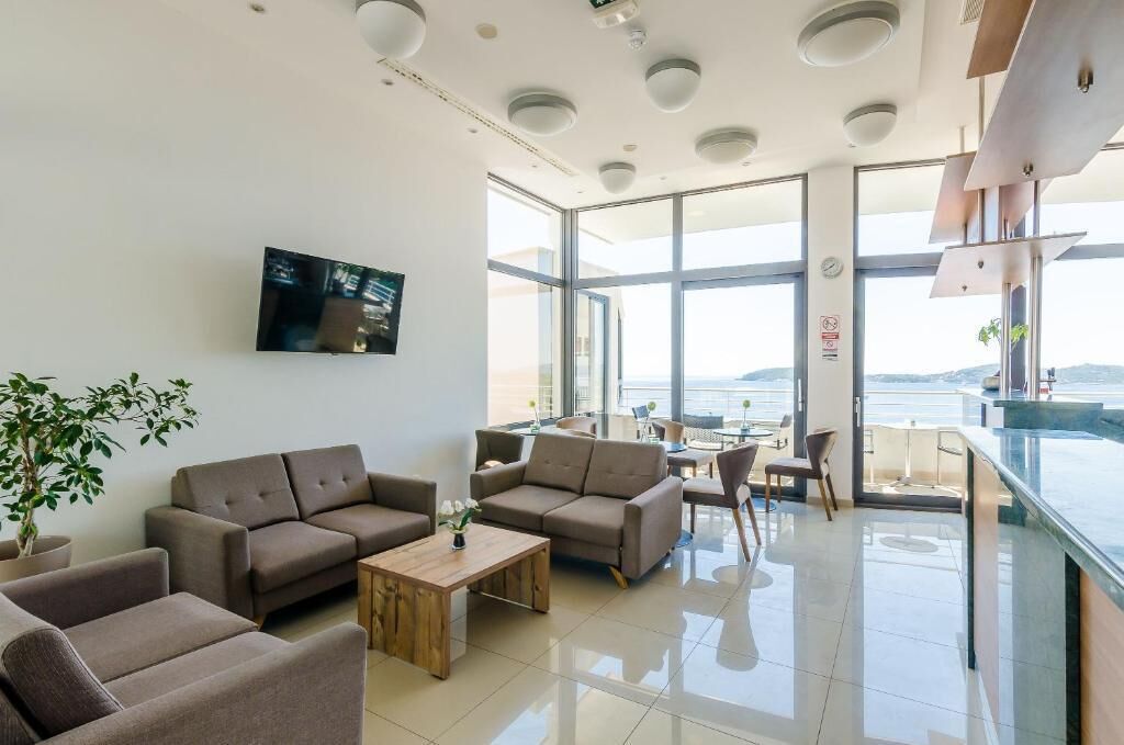 Un hall d’hôtel moderne avec des canapés, une table basse, un téléviseur et un balcon offrant une vue agréable.