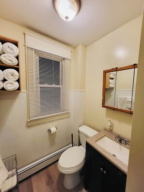 Une salle de bain avec des toilettes, un lavabo et une fenêtre équipée de stores.