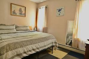 Une chambre à coucher avec un lit, une fenêtre avec des rideaux, un tableau au mur et un miroir.