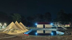 Escena nocturna con tiendas de campaña y una piscina.